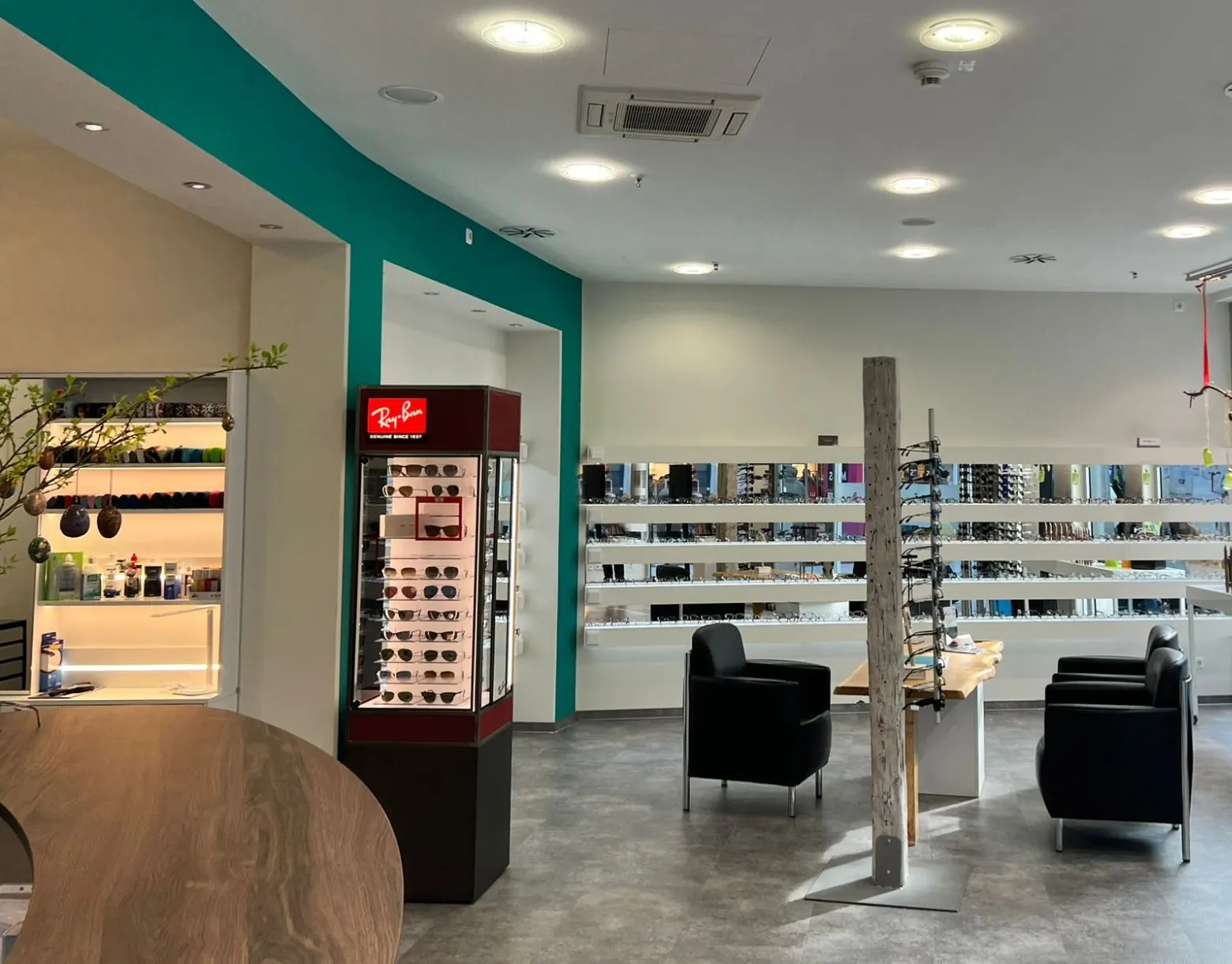 Blick in den Laden: Ray-Ban-Vitrine, lange Brillenwand, Sessel und Holztisch, dahinter die Schaufenster zum Ostsee Park